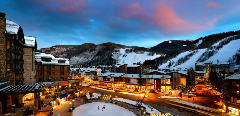 Snow-covered ski resort village at dusk with mountains in the background